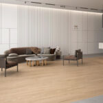 Contemporary lounge area with a curved gray sofa, two chairs, and a round marble coffee table on a light wood floor against white paneled walls.