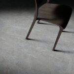 Dark wood chair tipped over on a gray tiled floor with dramatic lighting and shadows behind it.