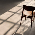 Empty wooden chair on a sunlit pale tile floor with long diagonal shadows across the ground.