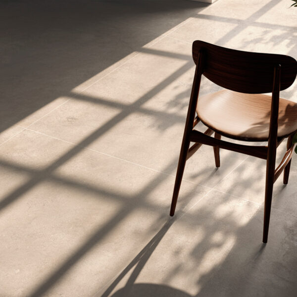 Empty wooden chair on a sunlit pale tile floor with long diagonal shadows across the ground.