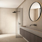 Modern bathroom with a glass-framed shower divider, round backlit mirror, wall-mounted faucet, and dark wood vanity.