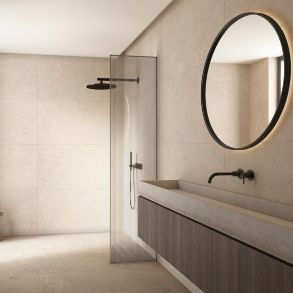Modern bathroom with a glass-framed shower divider, round backlit mirror, wall-mounted faucet, and dark wood vanity.