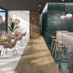 Modern cafe interior with white marble wall on the left, light wood flooring, and wicker chairs around wooden tables under woven pendant lights.
