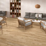 Living room with light wood floor, gray cushioned sofa, wooden armchairs, white coffee table, and a tall bookcase against a beige wall.