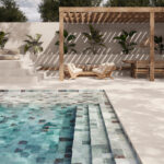 Poolside seating area under a wooden pergola with beige cushions and potted plants by the pool edge.
