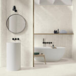 Modern bathroom with a freestanding white tub, round mirror, and black wall-mounted faucets on textured beige walls.