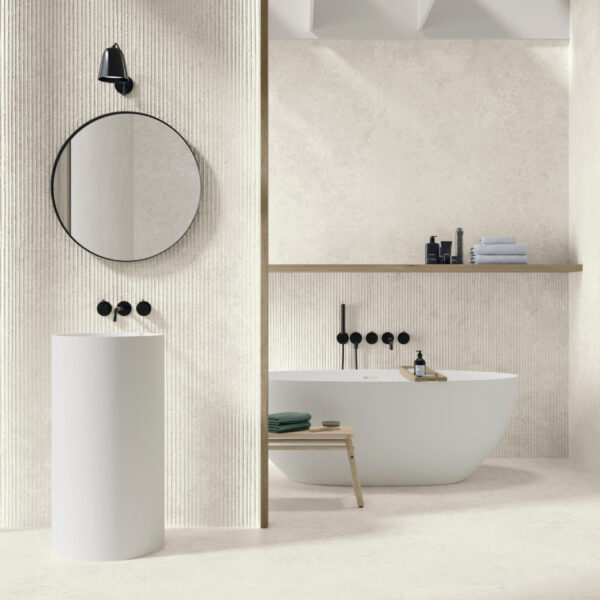 Modern bathroom with a freestanding white tub, round mirror, and black wall-mounted faucets on textured beige walls.