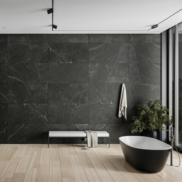 Contemporary bathroom with dark tiled wall, a black freestanding tub, a light wood floor, and a bench with a towel beside a potted plant near a large window.
