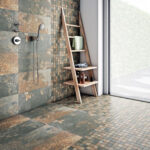 Modern bathroom shower area with stone tile walls and floor, chrome fixtures, and a wooden ladder shelf holding towels and bath products by a large window.