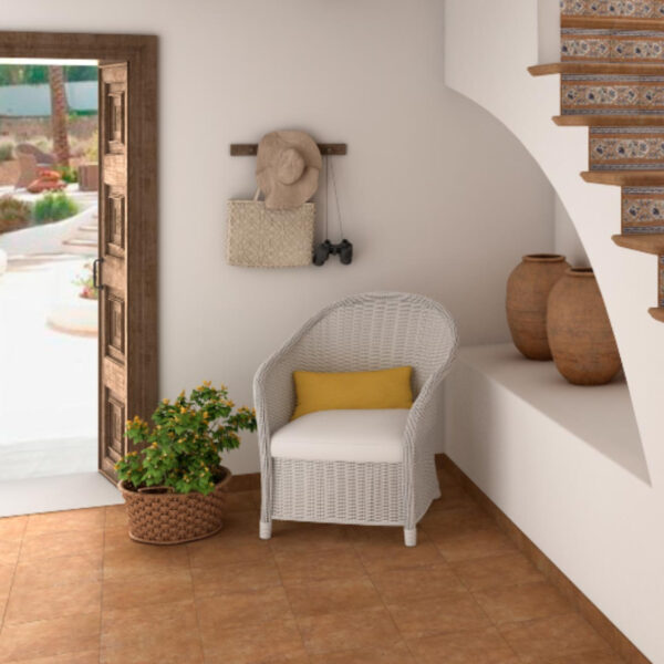 Bright entry alcove with white wicker chair and yellow cushion, a potted plant, wall hooks holding hat, bag, and binoculars, and an open wooden door to a sunny patio.