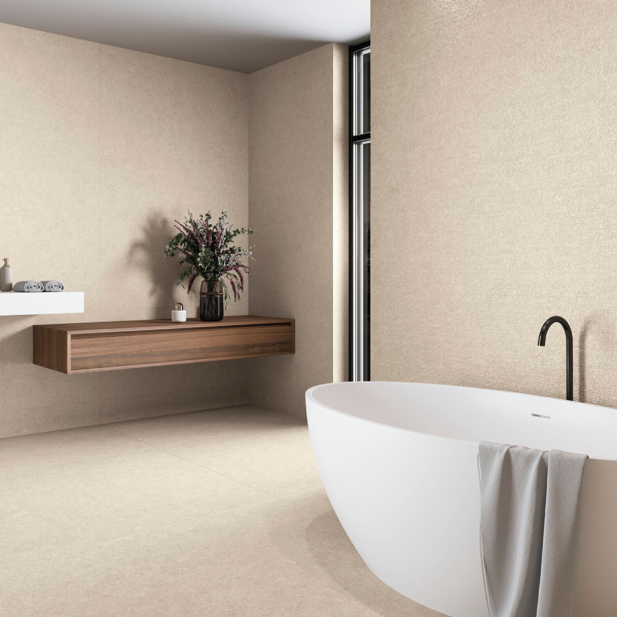 Minimalist bathroom with a white freestanding tub, black faucet, beige walls, and a wooden wall shelf with a vase of greenery.