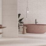 Modern bathroom scene featuring a pink freestanding bathtub, black faucet, hanging pendant lights, and a small wooden stool with towels beside a potted plant.