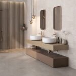 Modern bathroom with two round white vessel sinks on a floating beige vanity, bronze taps, and wavy textured wall