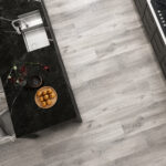 Top-down view of a kitchen with a black marble island, a sink, a plant, and a wooden plate of small round pastries on the counter next to light gray wood floors.