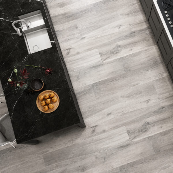 Top-down view of a kitchen with a black marble island, a sink, a plant, and a wooden plate of small round pastries on the counter next to light gray wood floors.