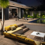 Modern night-time backyard with a illuminated pool, wooden deck, and yellow-cushioned seating surrounding a white coffee table and lounge chairs.
